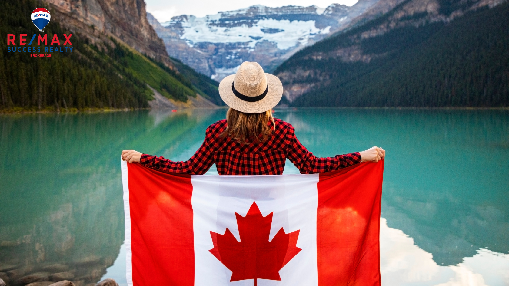 person holding canadian flag behind their back looking out on a lake with mountains