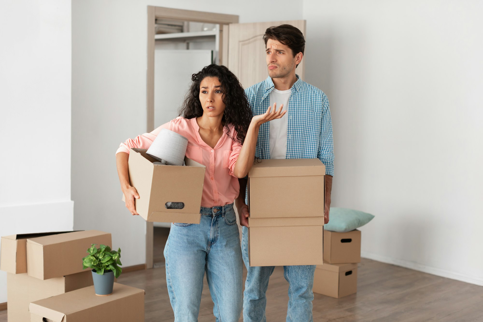 Confused couple holding cardboard boxes learning about what real estate mistakes to avoid